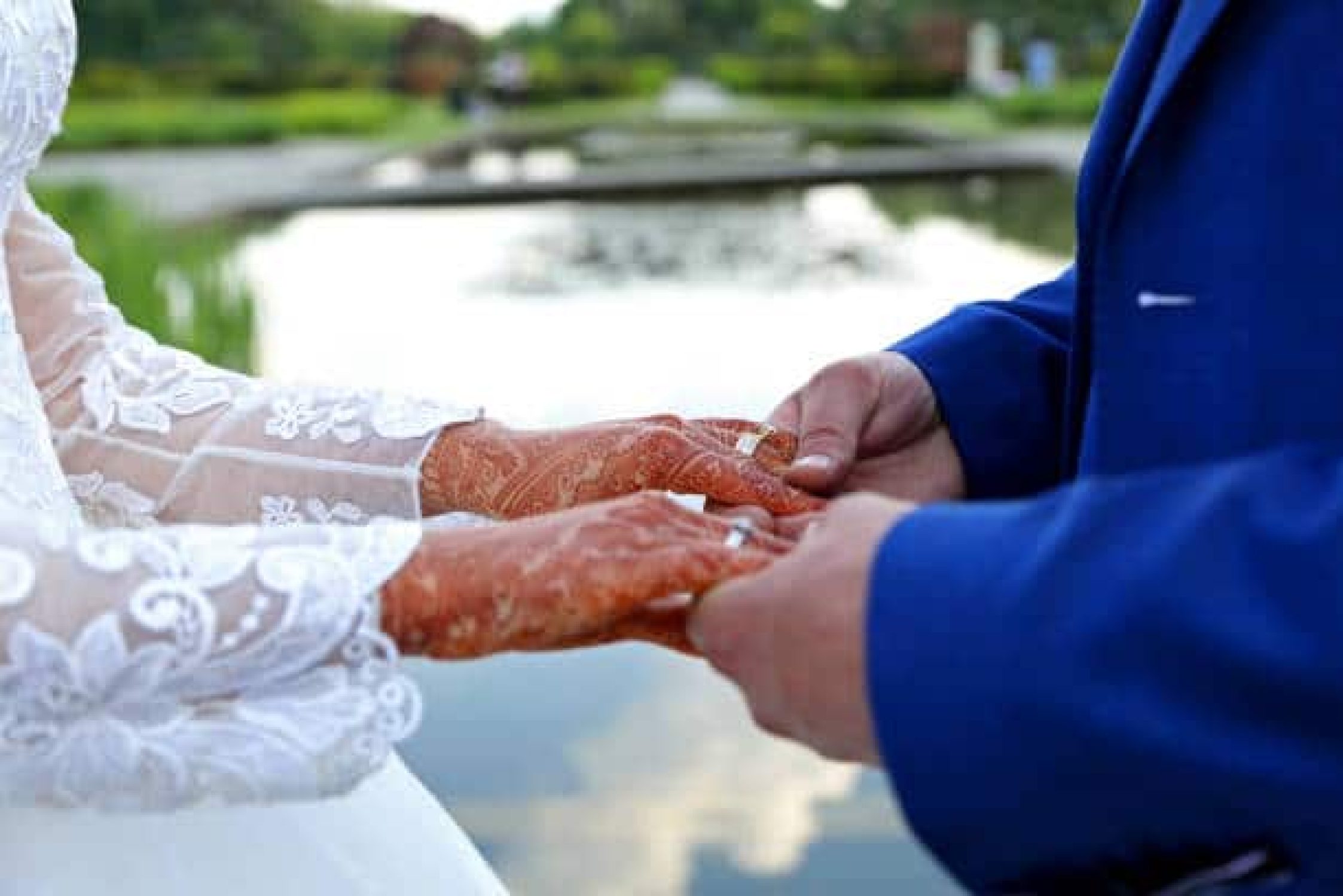 A groom holds the bride's hand. The bride's hand is decorated with henna tattoos.